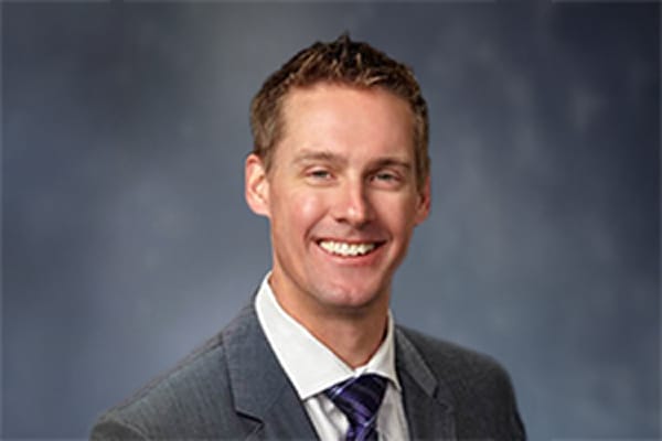 Smiling man in a suit and tie against a gray background.