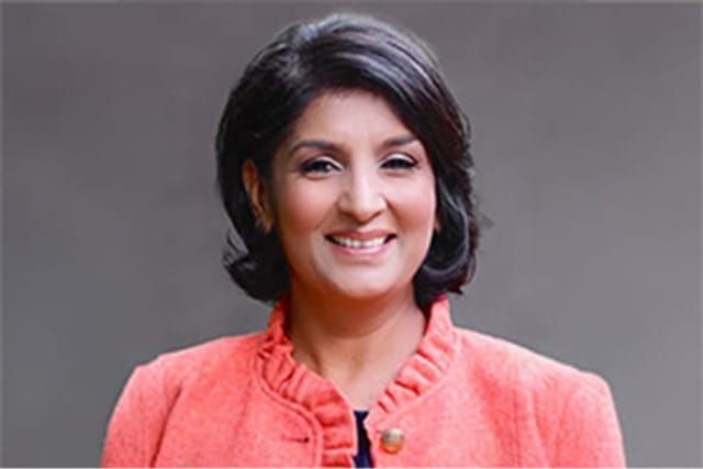 Person smiling while wearing a coral-colored jacket against a gray background.