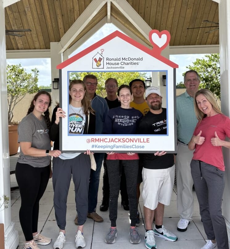 A group of Treace employees posing behind a Ronald McDonald House Charities Jacksonville photo frame during a community service event.