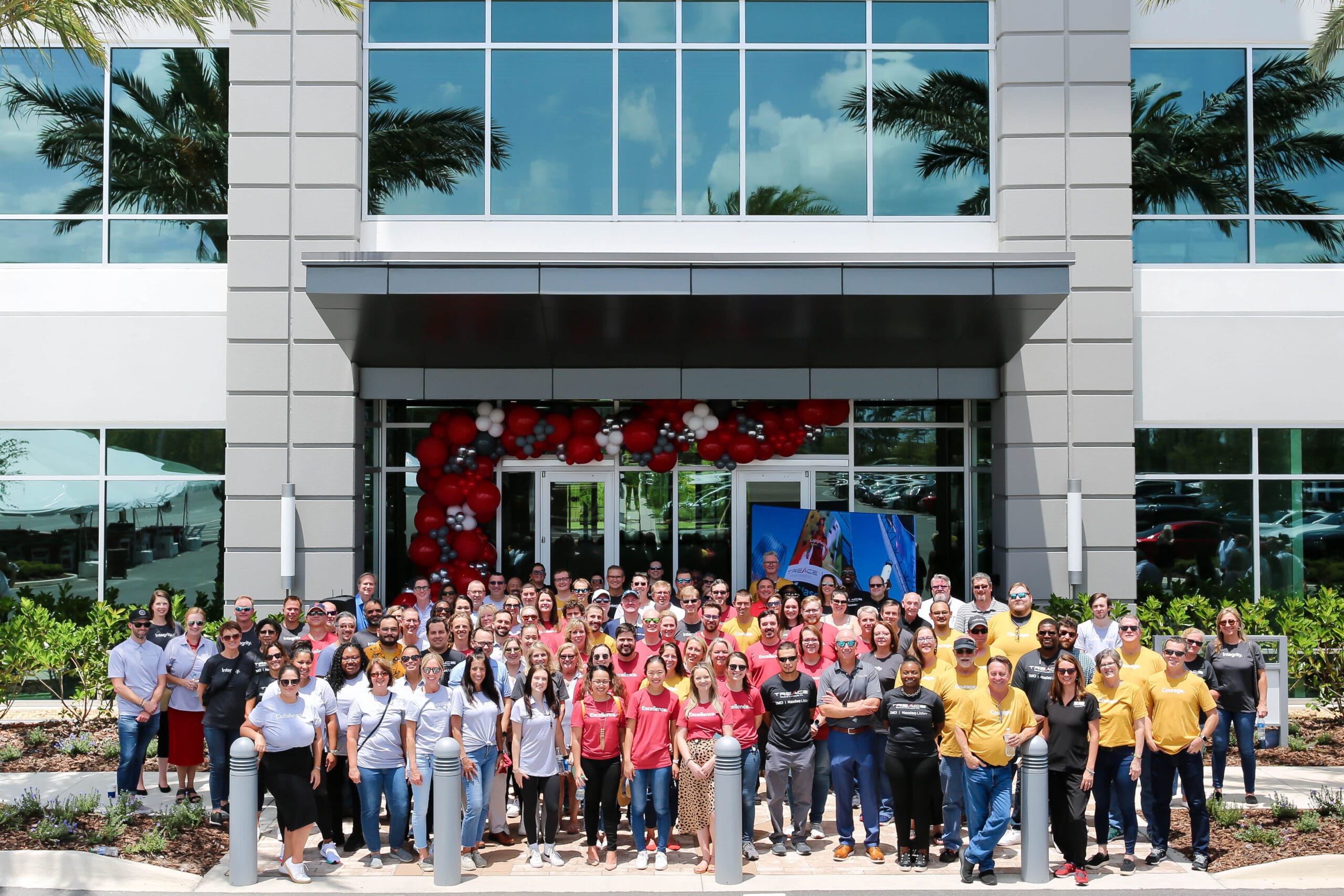 Large group of people standing in front of a building with red balloons above the entrance.