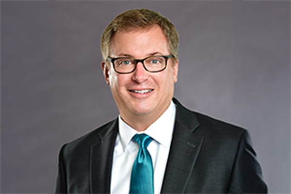Man in a suit and tie smiling against a gray background