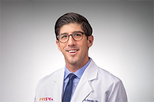 Doctor smiling in a white coat with a light gray background.