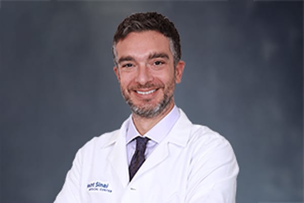 A medical professional in a white coat smiling with a neutral background.