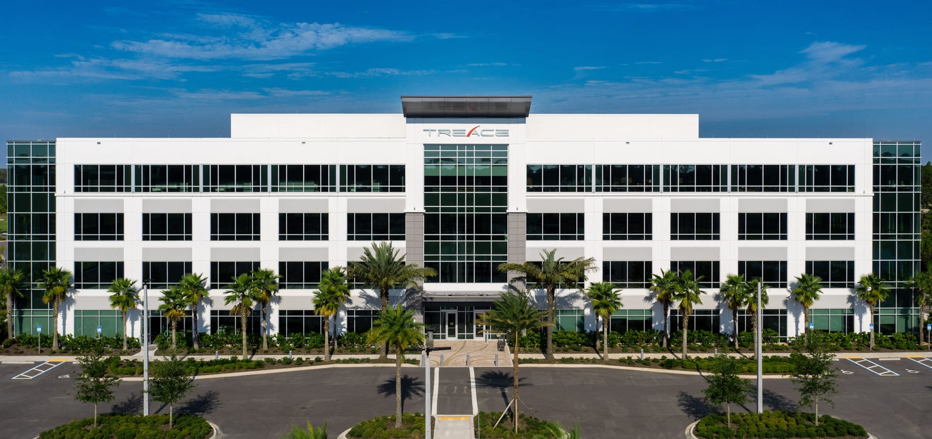 Exterior view of the Treace Medical Concepts corporate headquarters, a modern white four-story office building with large glass windows and palm trees.