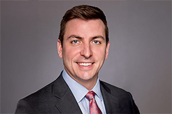 Smiling man in a suit and tie against a gray background.