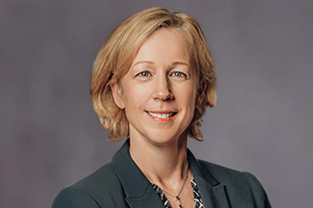 Smiling person in a professional blazer against a gray background