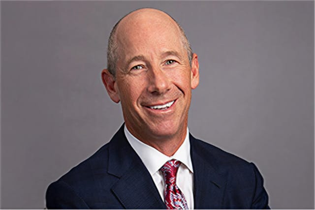 Smiling man in a suit and tie against a gray background.