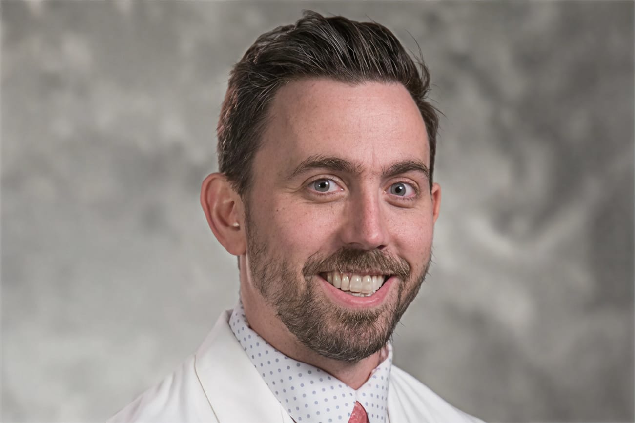 Smiling man in a white coat against a gray background