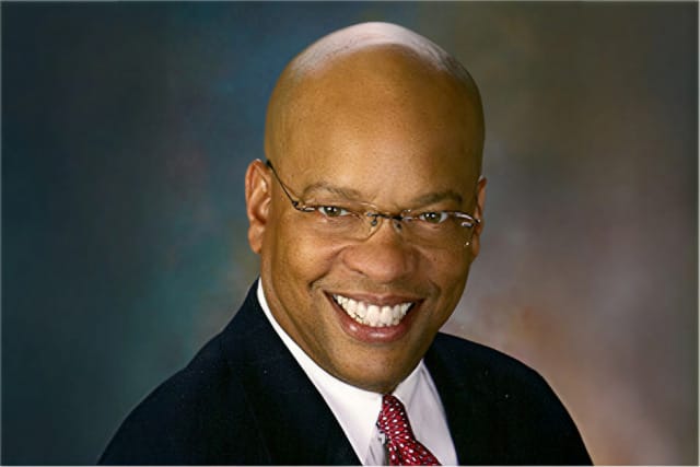 Smiling person in a suit and tie with a blurred background.