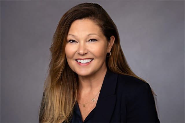 Smiling woman with long hair in business attire against a grey background.