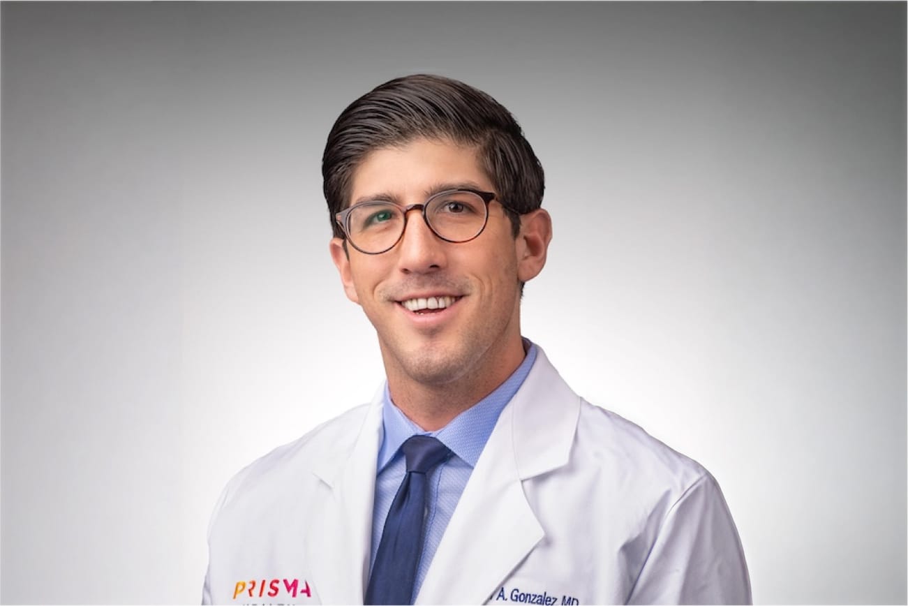 Smiling man in a white coat and glasses against a plain background.