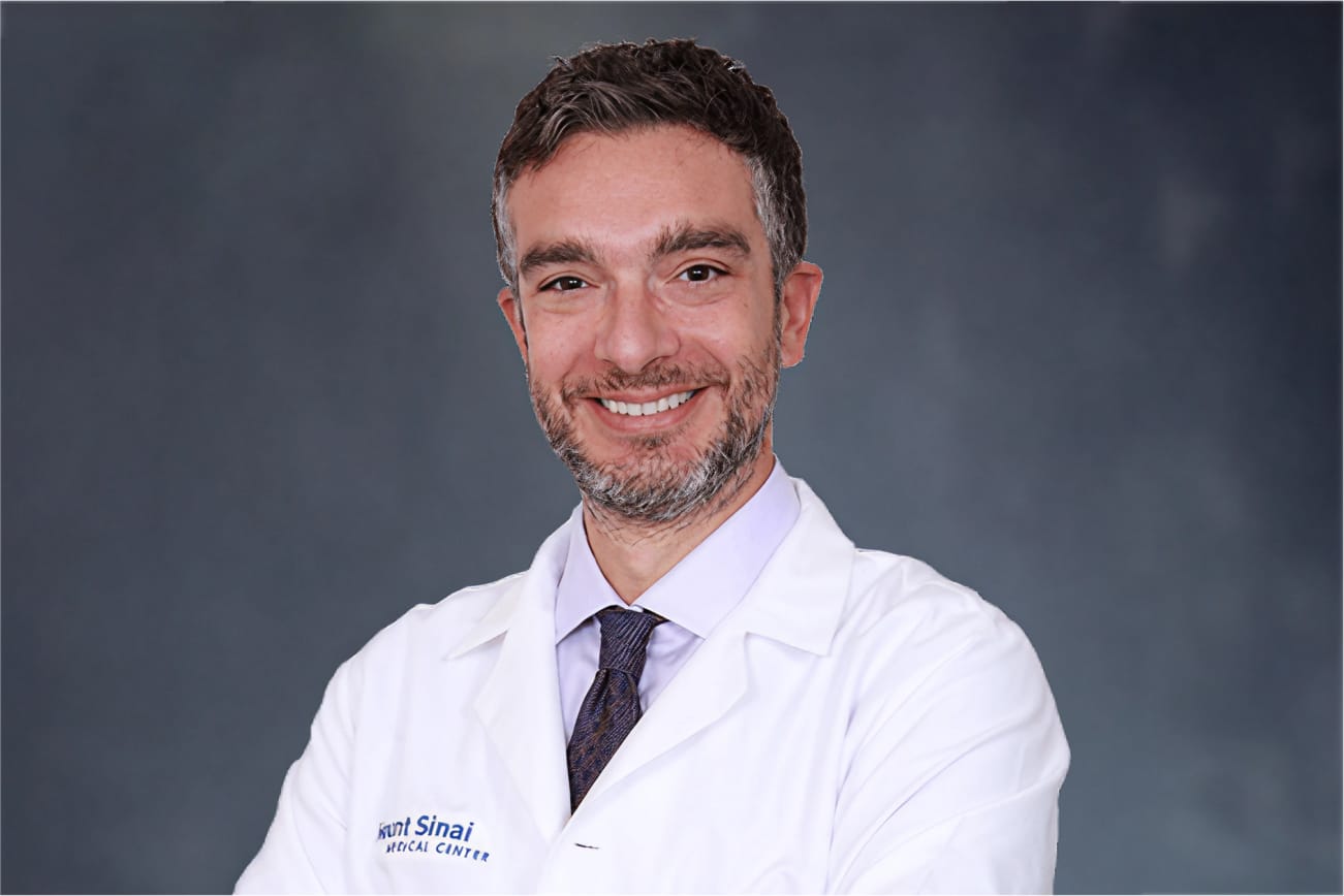 Doctor in white lab coat smiling against a dark background.