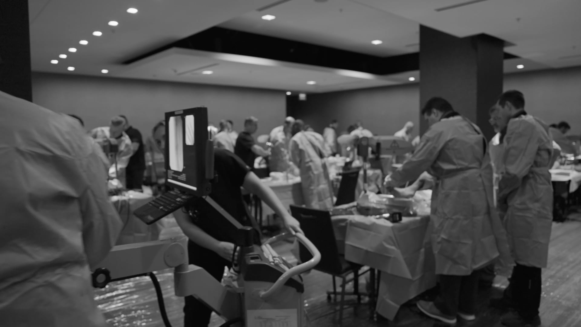 Healthcare professionals in surgical gowns participating in a hands-on medical training lab with surgical equipment and monitoring stations.