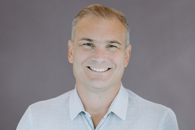 Smiling person in a light-colored shirt against a plain background.